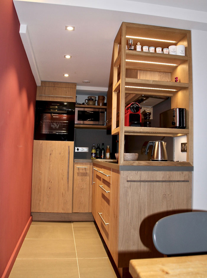 La cuisine avec meubles en chênes claires est reliée visuellement au coin repas grâce aux étagères en têtes de plan de travail