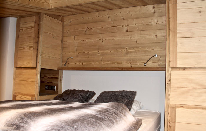 La tête de lit en mezzanine intègre le parement bois du mur, deux volumes de rangement de part et d'autre et deux niches servants de chevets.